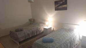 Ein Schlafzimmer mit zwei Einzelbetten, einem Nachttisch mit Lampe, einem Wandbild und einem kleinen Tisch.