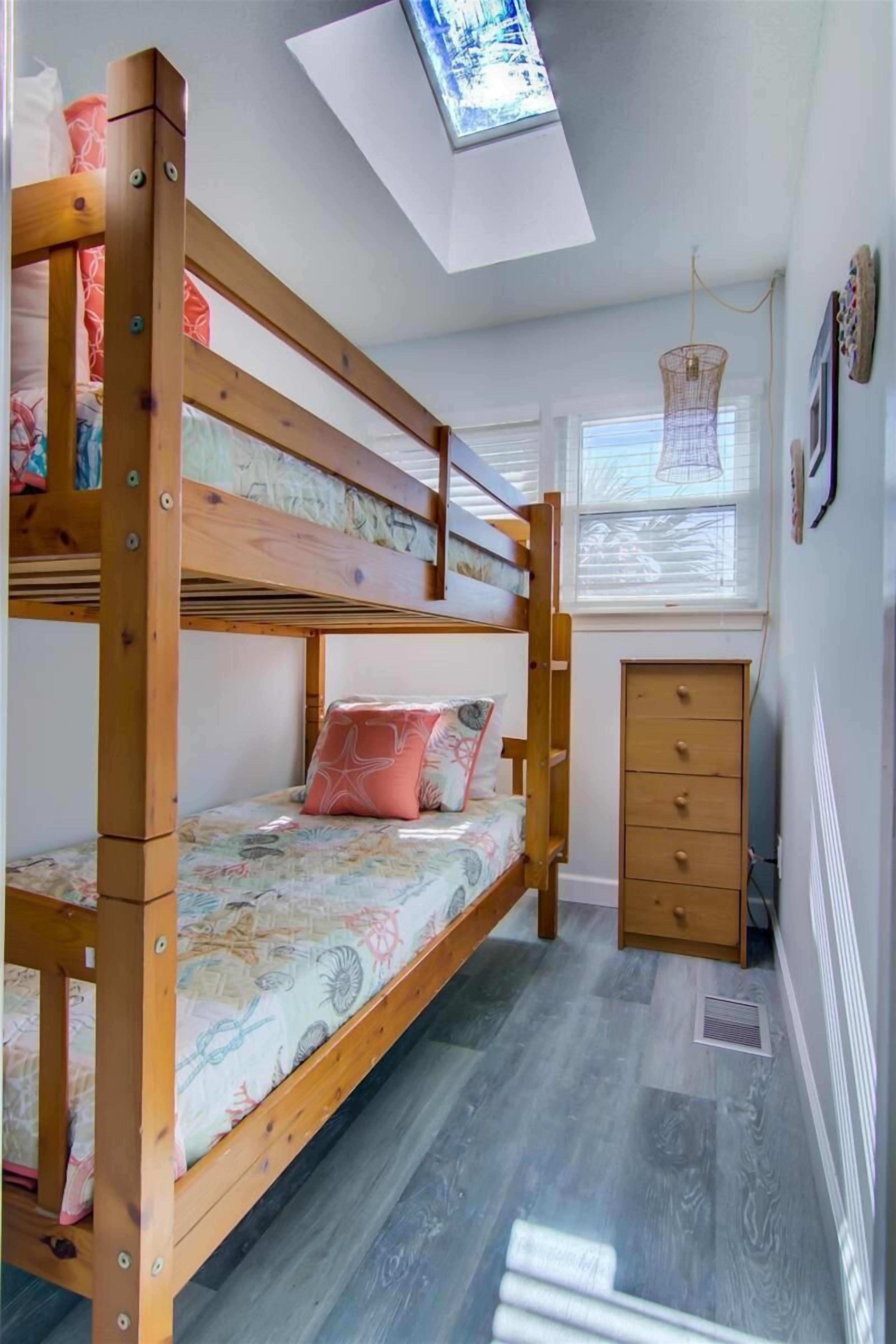 A bunk bed room with a skylight, a hanging light fixture, and a window with blinds.