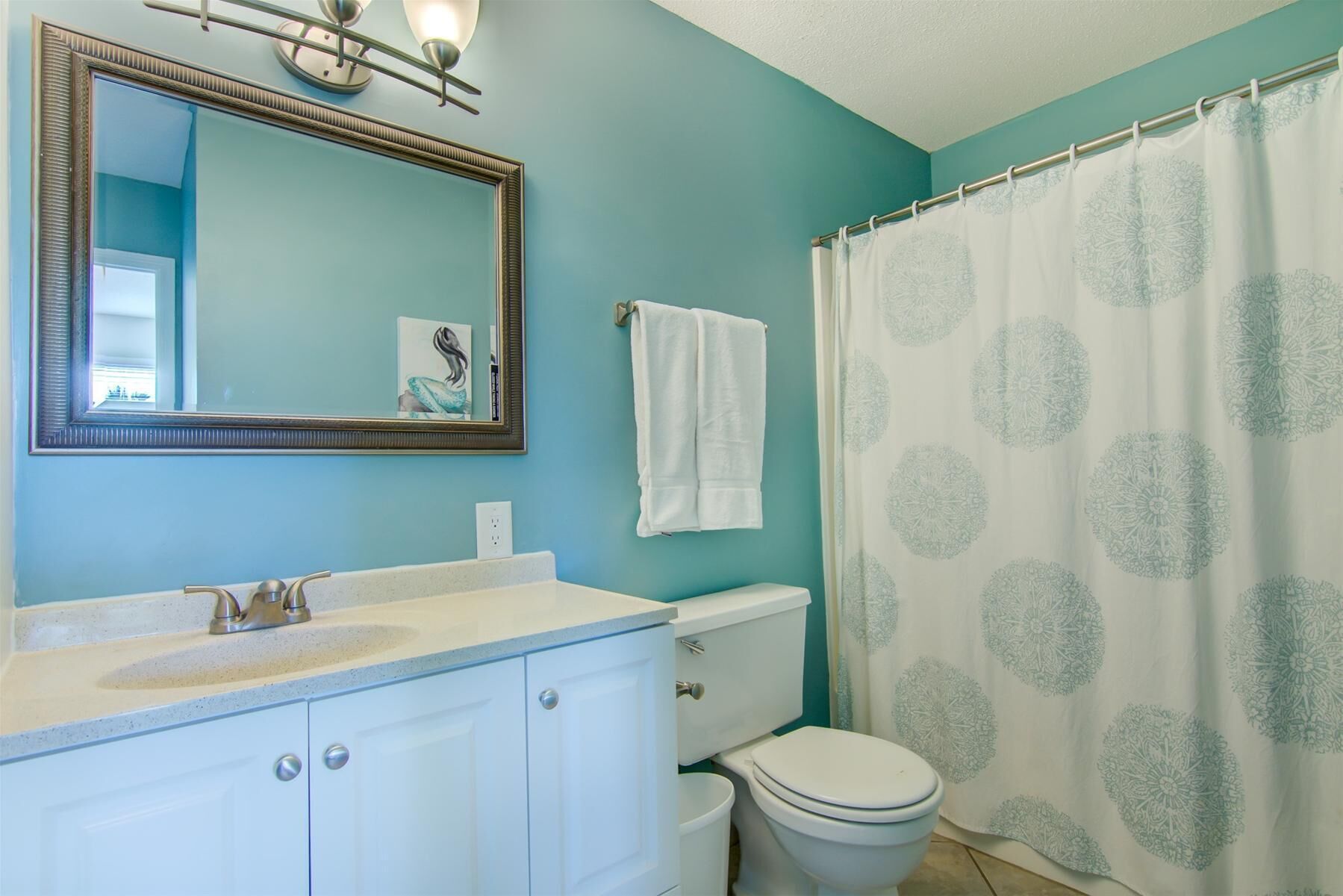 Une salle de bain avec un meuble-lavabo blanc, des toilettes et un rideau de douche orné d’un motif circulaire.