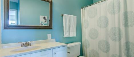 Une salle de bain avec un meuble-lavabo blanc, des toilettes et un rideau de douche orné d’un motif circulaire.