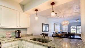 A kitchen with granite countertops, white cabinets, stainless steel appliances, and pendant lighting. - 2B, Fore Shore! (Miramar Beach)