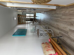 A room with a wooden floor, a blue mat, a bed with a metal frame, a wooden bench, and a woven rug.
