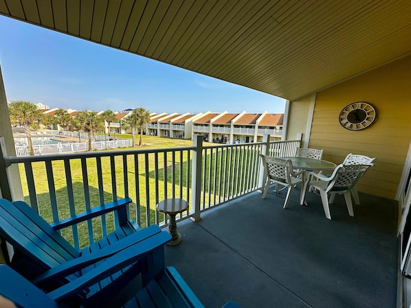 A balcony with a view of a pool and buildings, a table with chairs, and a clock on the wall.