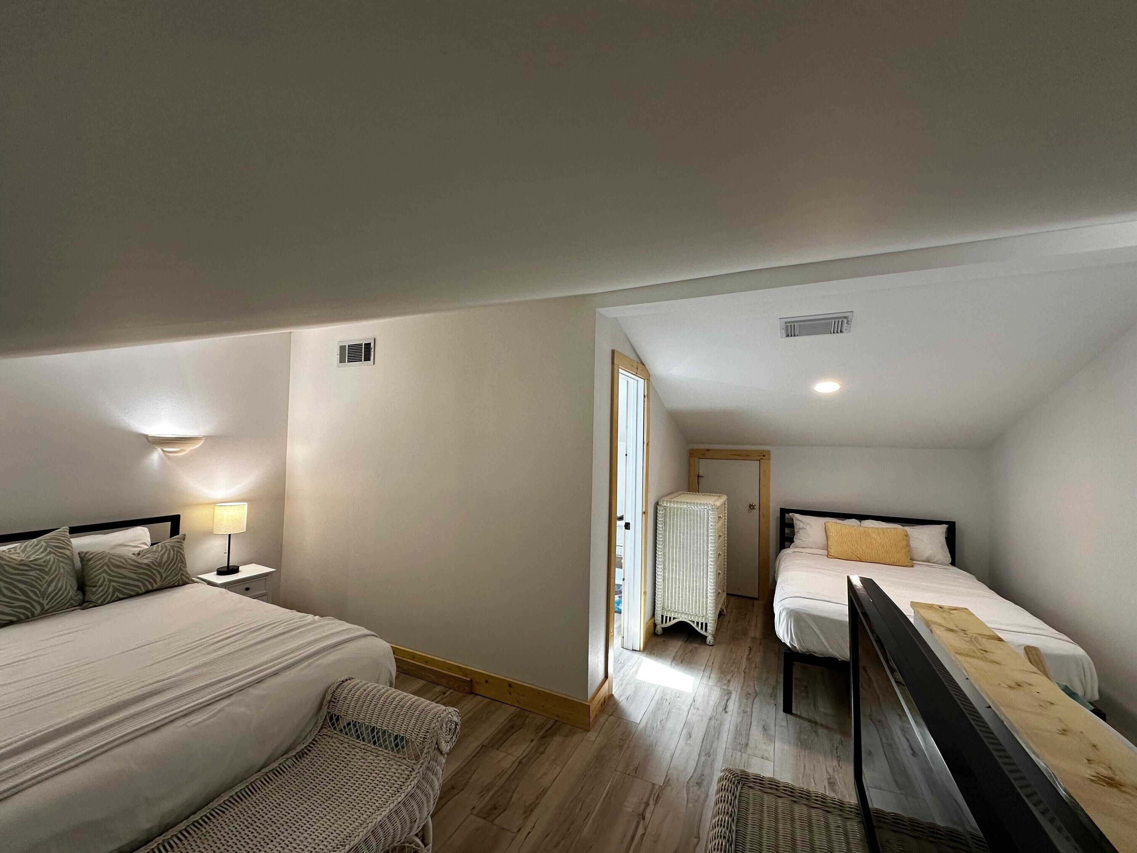 A bedroom with two beds, a nightstand, a lamp, a radiator, and a wooden floor.