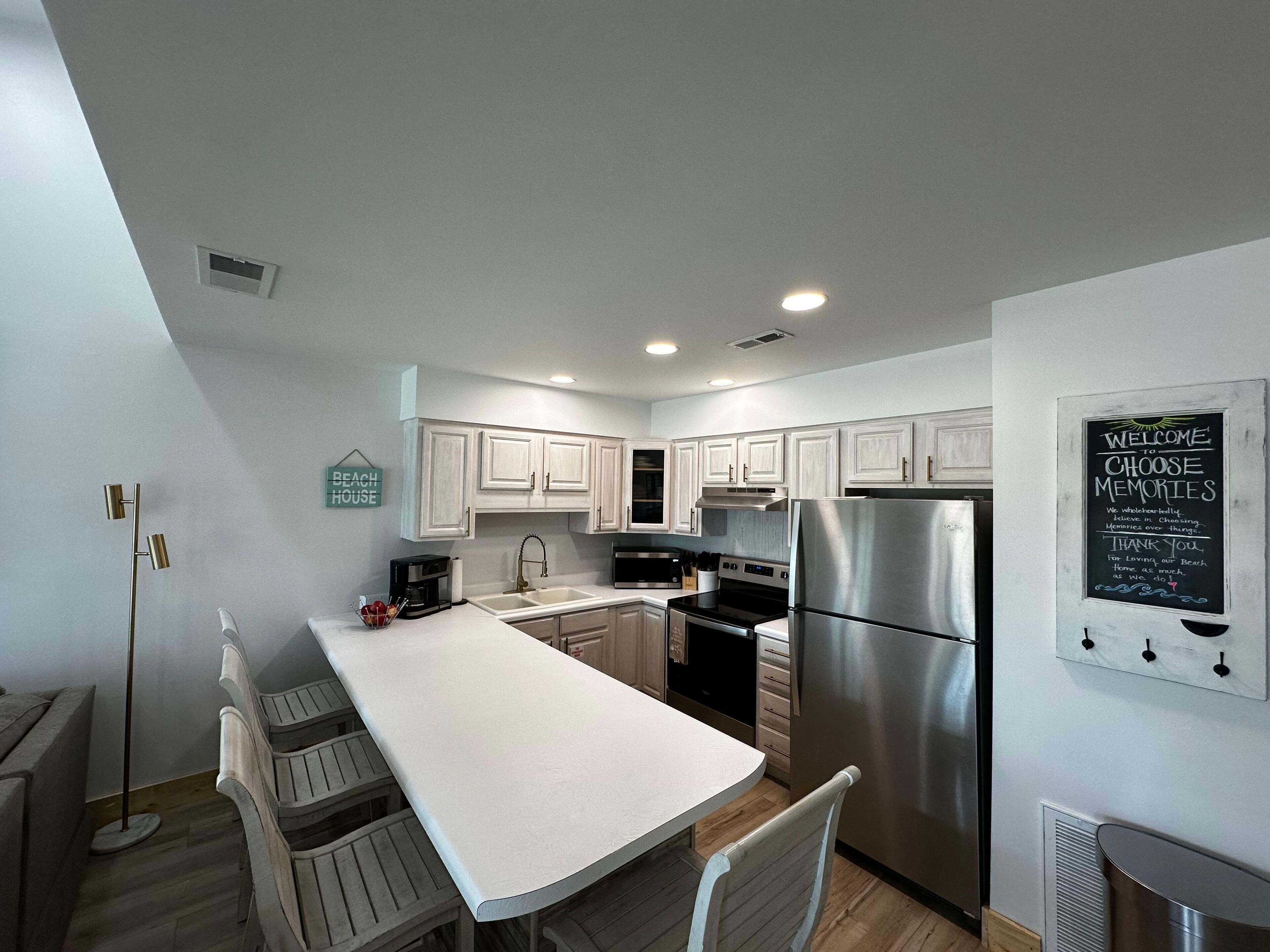 A modern kitchen with white cabinets, a stainless steel refrigerator, and a chalkboard sign.