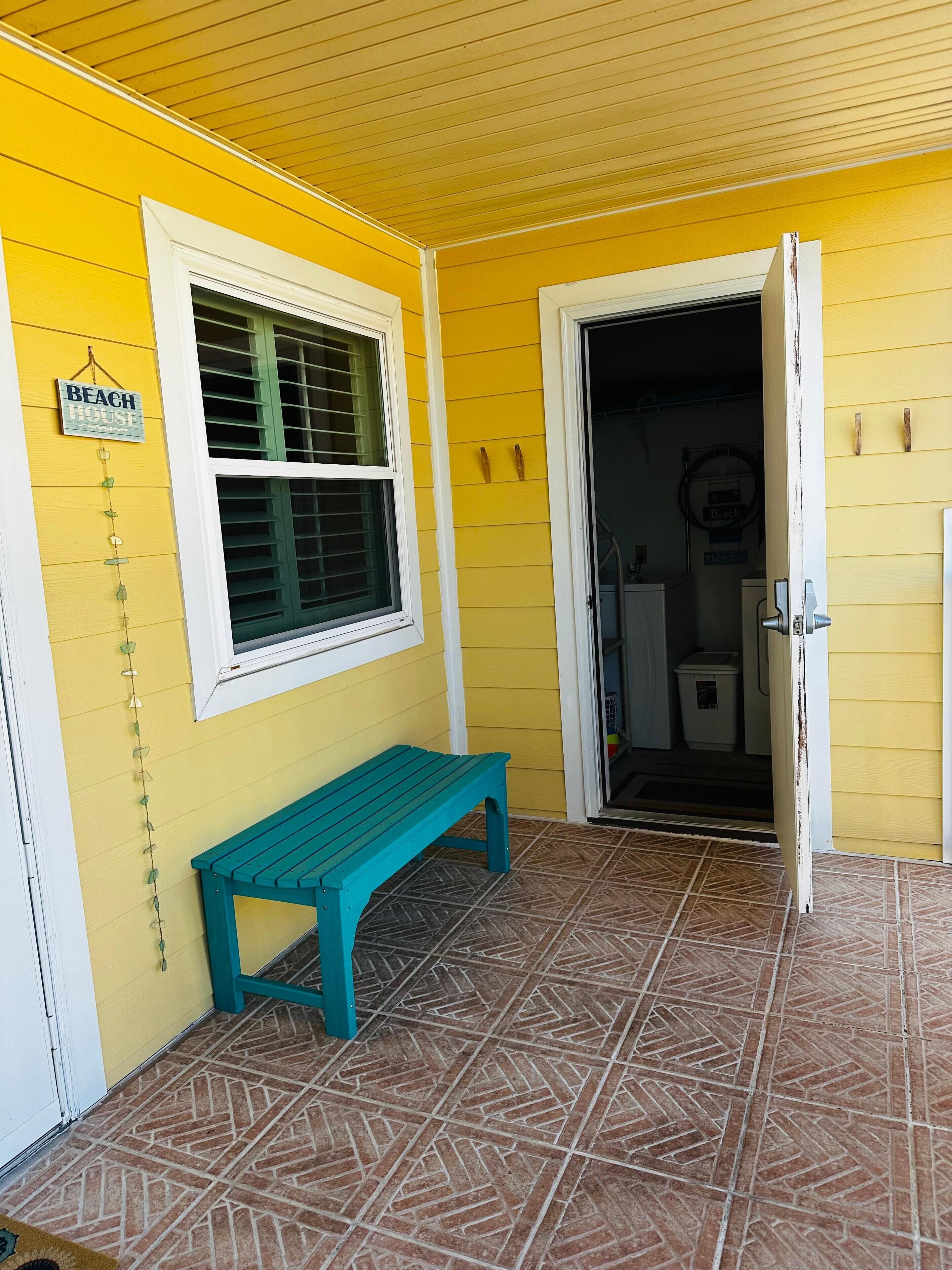 A yellow building with a 'Beach House' sign, a green bench, and a patterned tile floor.