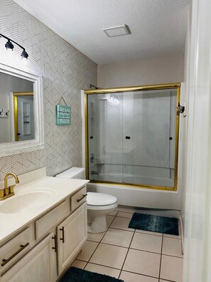 A bathroom with a white sink, gold faucet, and a glass-enclosed shower with a gold frame.