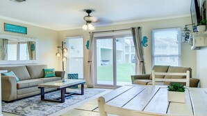 A spacious living room with a sofa, a coffee table, and a wooden bench. There is a sliding glass door leading to a balcony with a view of the outdoors. - 7A, Vacay All Day (Miramar Beach)
