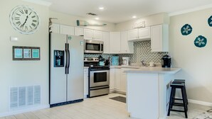 A modern kitchen with white cabinets, stainless steel appliances, a central island, and decorative wall art. - 7A, Vacay All Day (Miramar Beach)