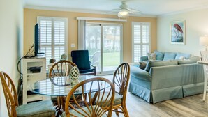 A living room with a glass-top dining table, wooden chairs, a blue sofa, and a ceiling fan. - 7 D, One Bedroom Condo (Destin)