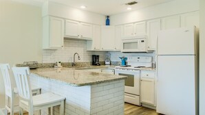A kitchen with white cabinets, a granite countertop, a sink, a stove, a microwave, and a refrigerator. - 7 D, One Bedroom Condo (Destin)