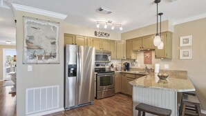 A modern kitchen with stainless steel appliances, wooden cabinets, and a central island with bar stools. - 8 G Two Bedroom Condo (Miramar Beach)