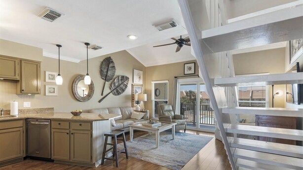 A spacious kitchen with wooden cabinets, a dining area with a white table and chairs, and a staircase leading to a balcony. - 8 G Two Bedroom Condo (Miramar Beach)
