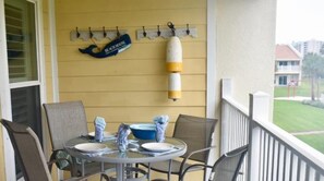 A balcony with a table set for two, chairs, a wall-mounted buoy, and a sign reading "Beach House". - 9 H Two Bedroom Condo (Miramar Beach)