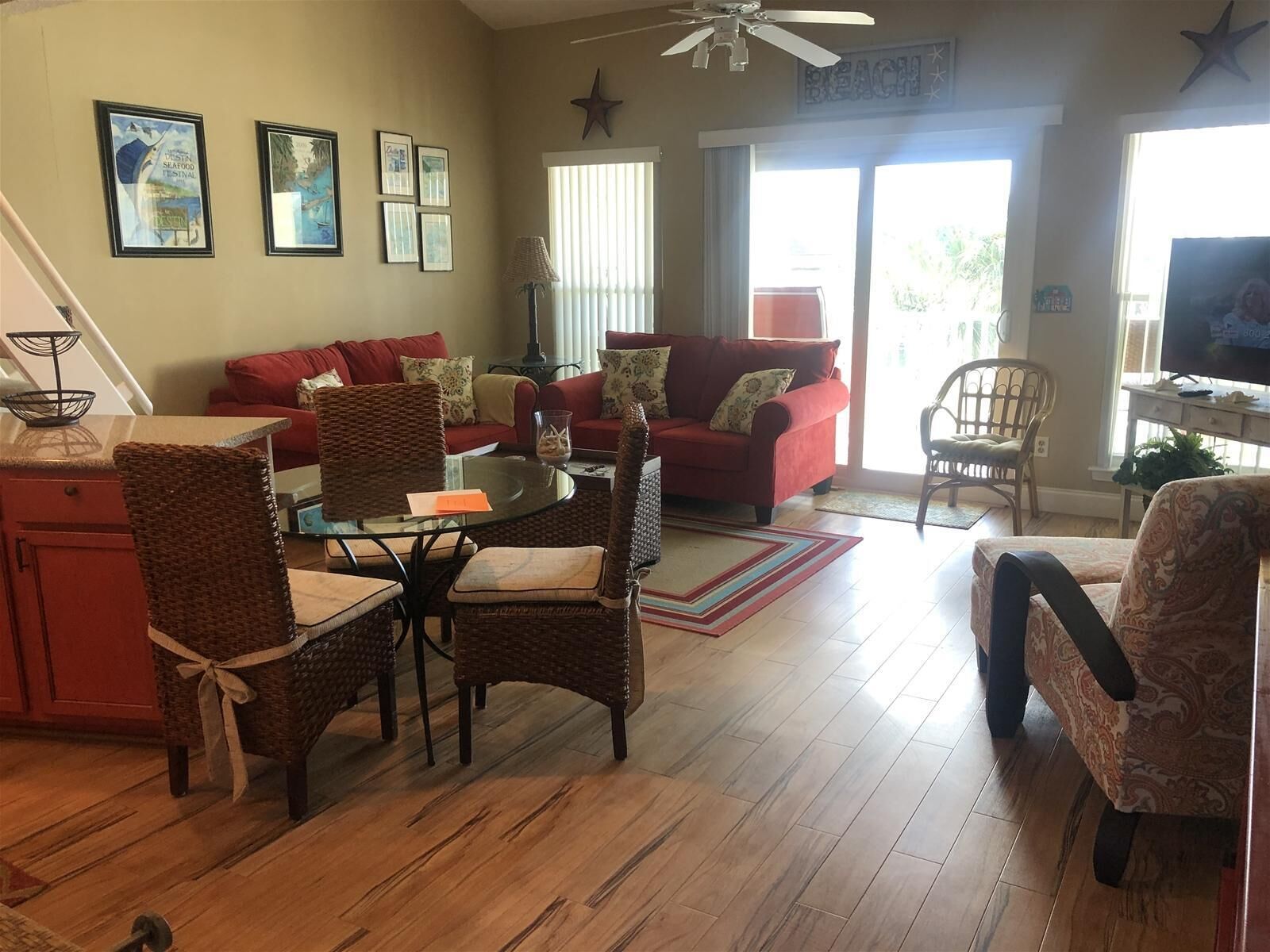 A cozy living room with a red sofa, wicker chairs, a glass coffee table, and a television.