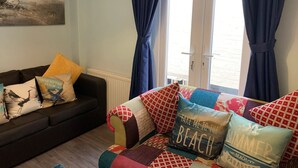 Un salon avec un canapé et des fauteuils, un tableau accroché au mur et une vue par une fenêtre ornée de rideaux.