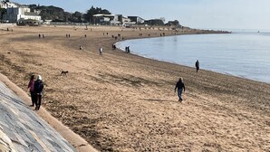 Une vaste plage de sable où l’on voit des gens se promener, avec quelques bâtiments en arrière-plan.