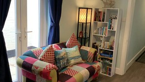 Un salon chaleureux avec un canapé aux motifs colorés, une bibliothèque et une grande fenêtre agrémentée de rideaux.