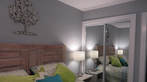 A bedroom with a wooden headboard, a bed with patterned bedding, two bedside lamps, and a mirror reflecting the room. - 10e, Our Happy Place (Miramar Beach)