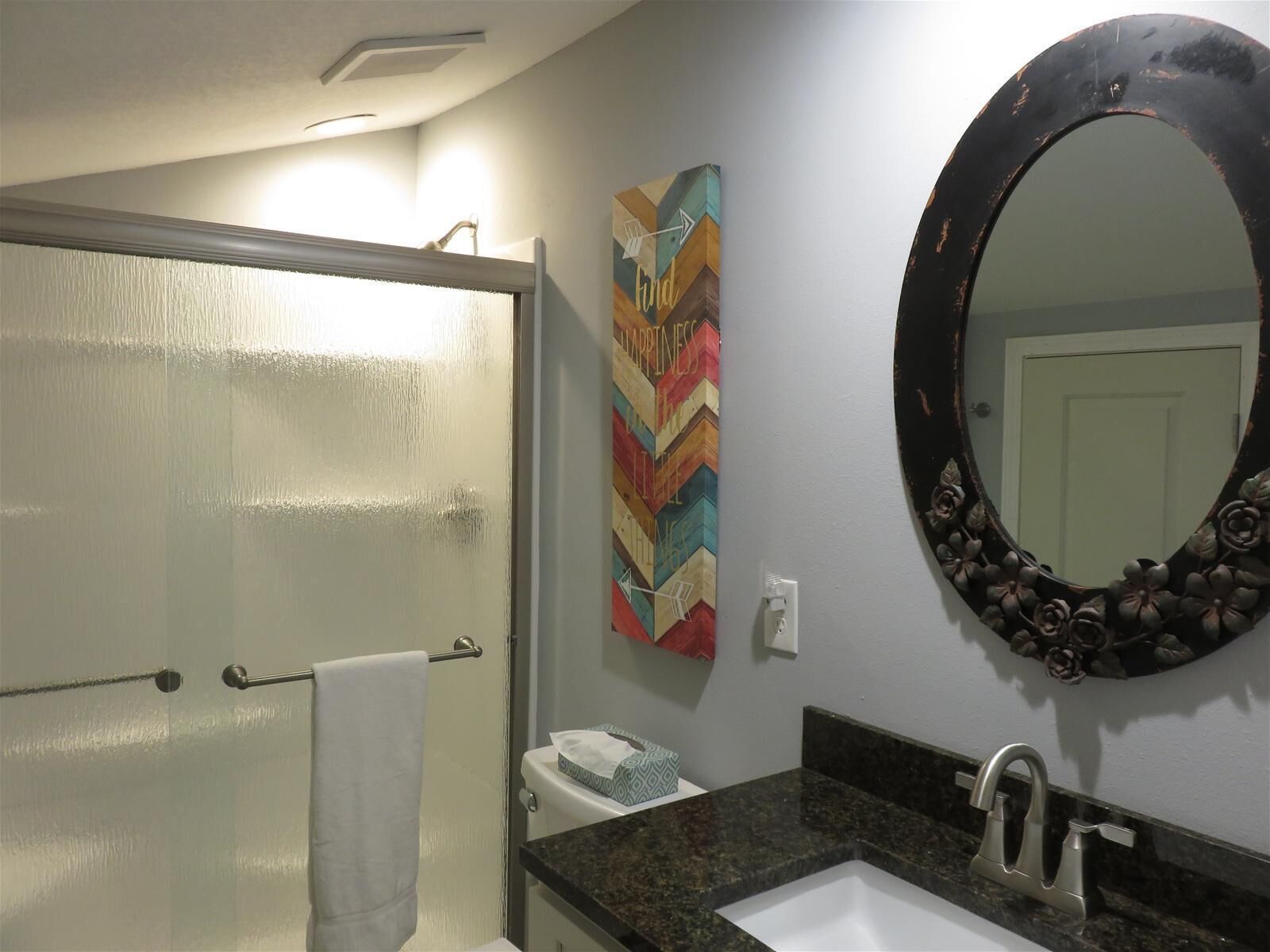 A bathroom with a white sink, a large mirror, and a colorful artwork on the wall.