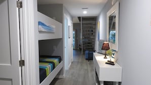 A narrow hallway with a bunk bed on the left, a desk with a lamp on the right, and a bookshelf in the background. - 10e, Our Happy Place (Miramar Beach)