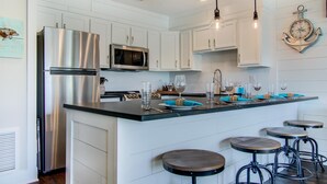 A modern kitchen with white cabinetry, stainless steel appliances, and a central island with bar stools. - Settle on the Sand (Miramar Beach)