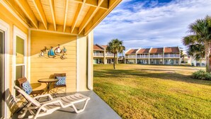A hotel with a covered outdoor seating area, a lawn, and multiple-story buildings in the background. - Settle on the Sand (Miramar Beach)