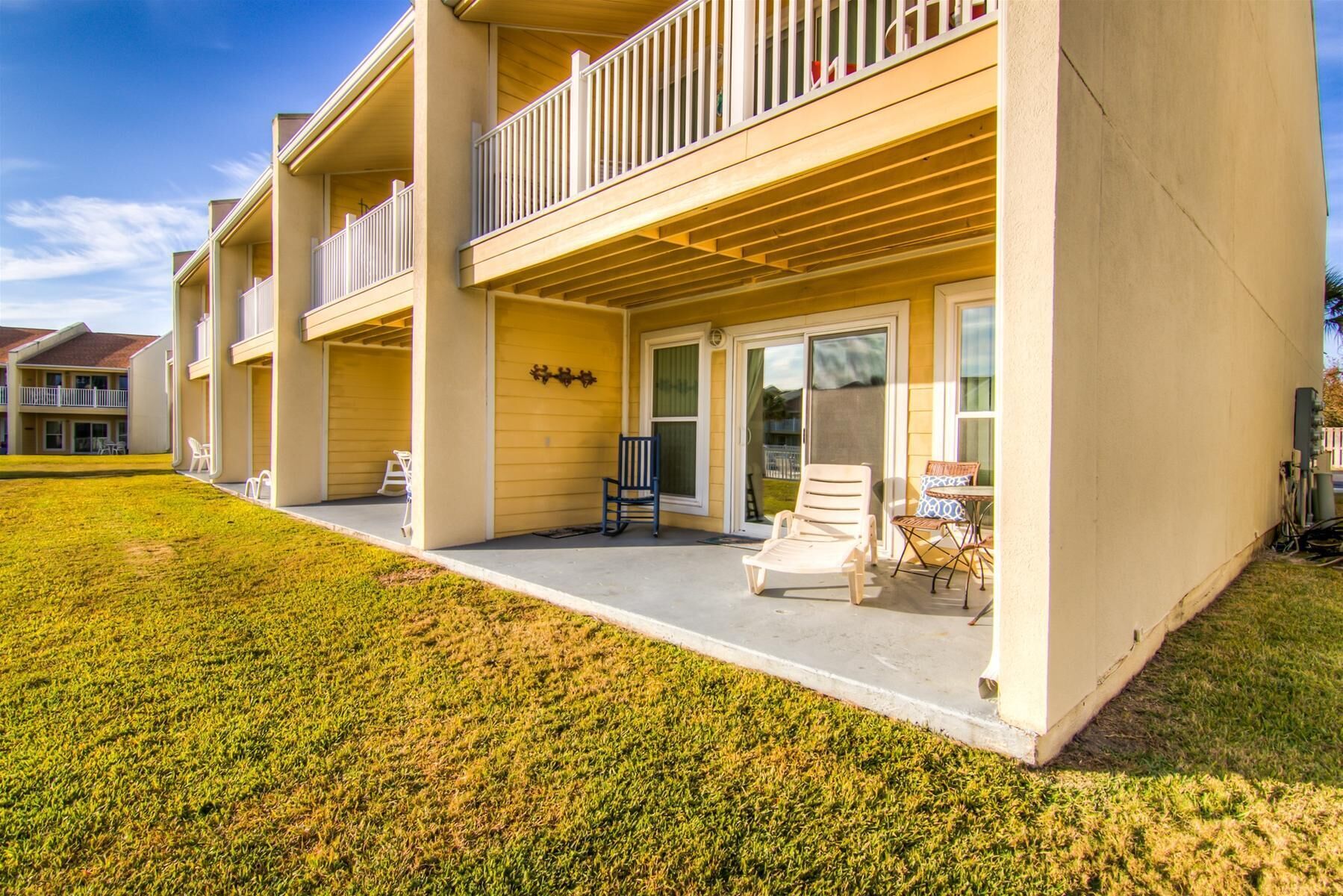 A multi-story residential building with a covered patio area, outdoor seating, and a well-maintained lawn.