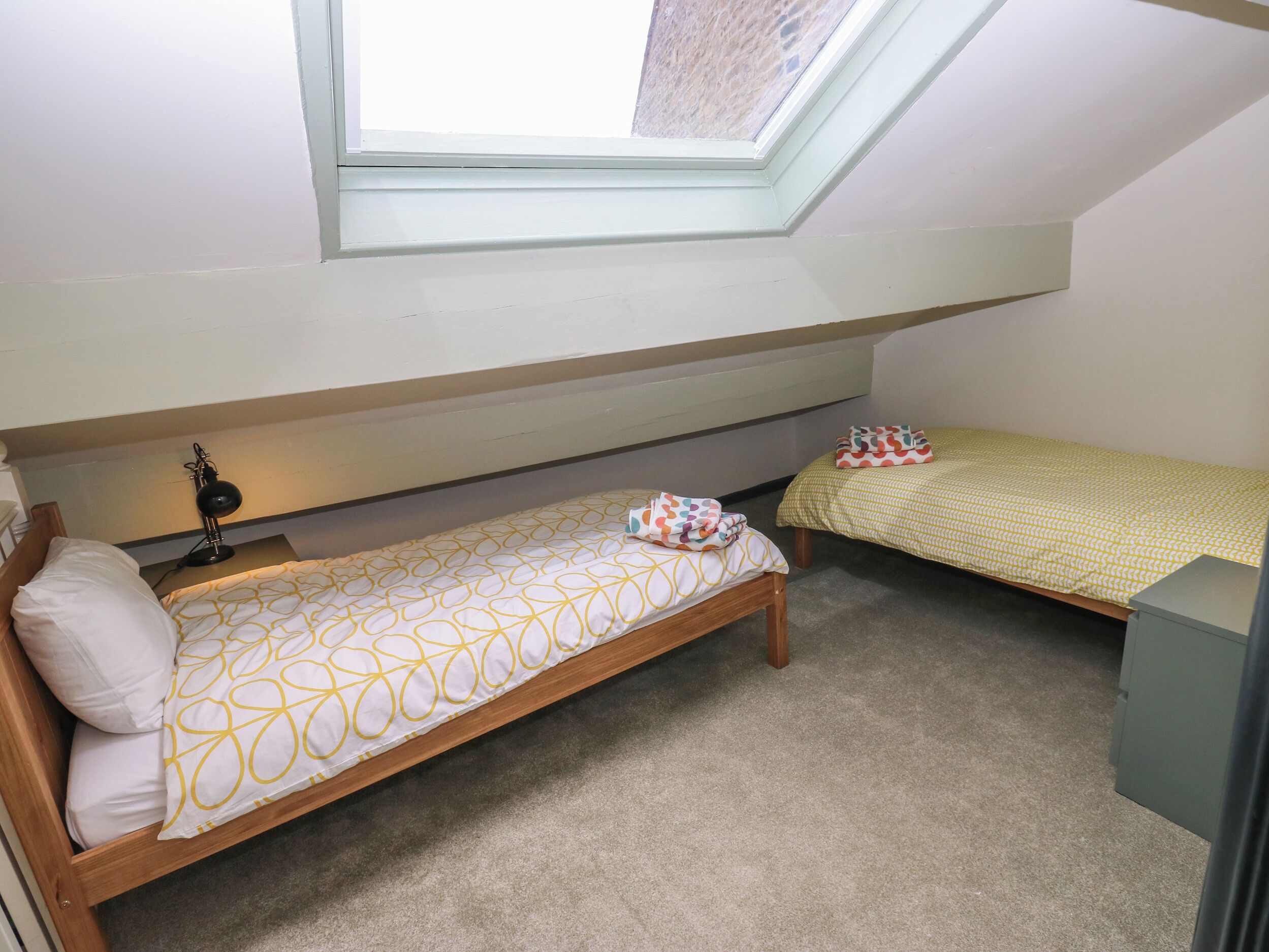 A small, single-room accommodation with two single beds, a skylight, and a desk.