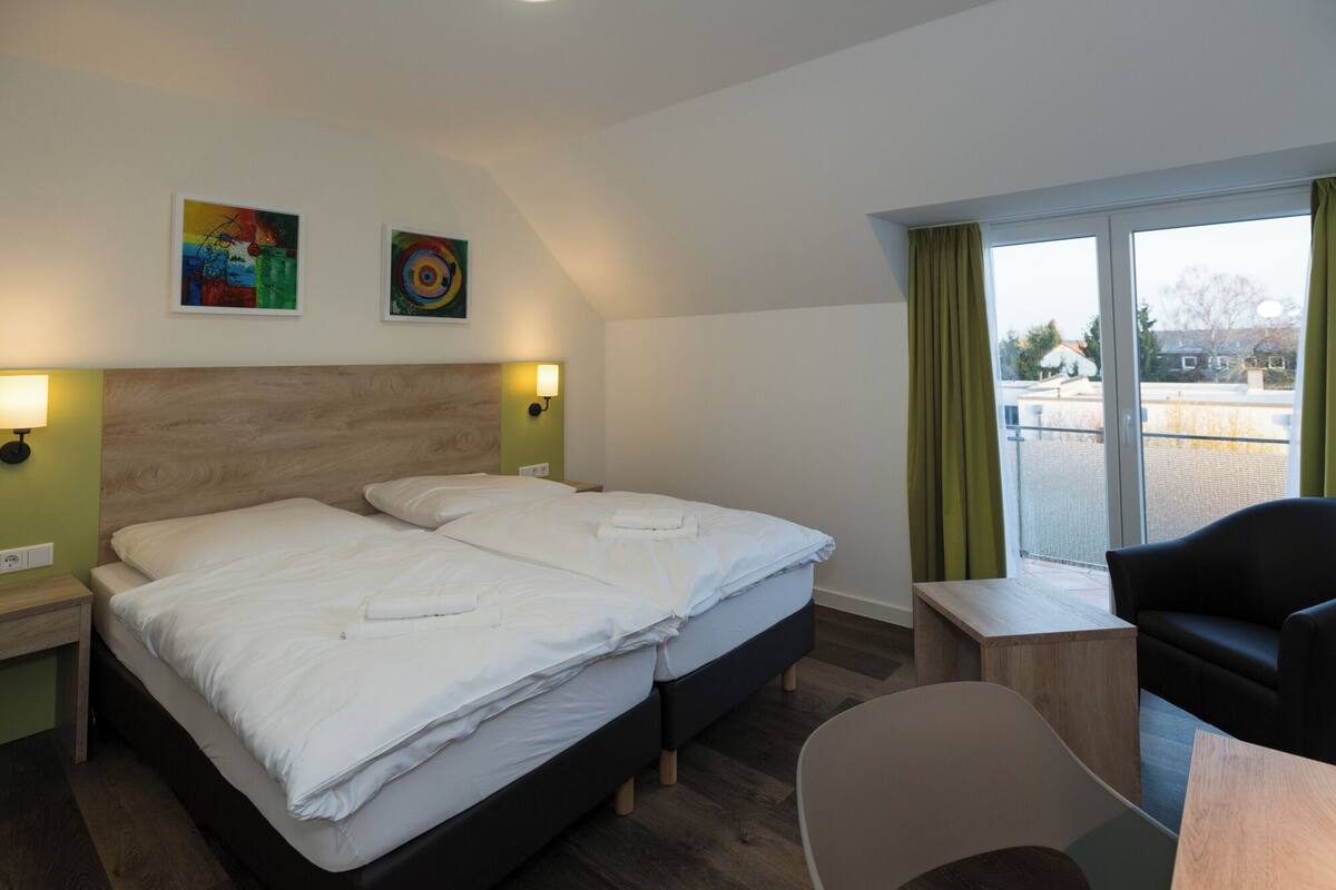 A hotel room with a double bed, two wall-mounted lamps, a small table, a chair, and a balcony with a view.