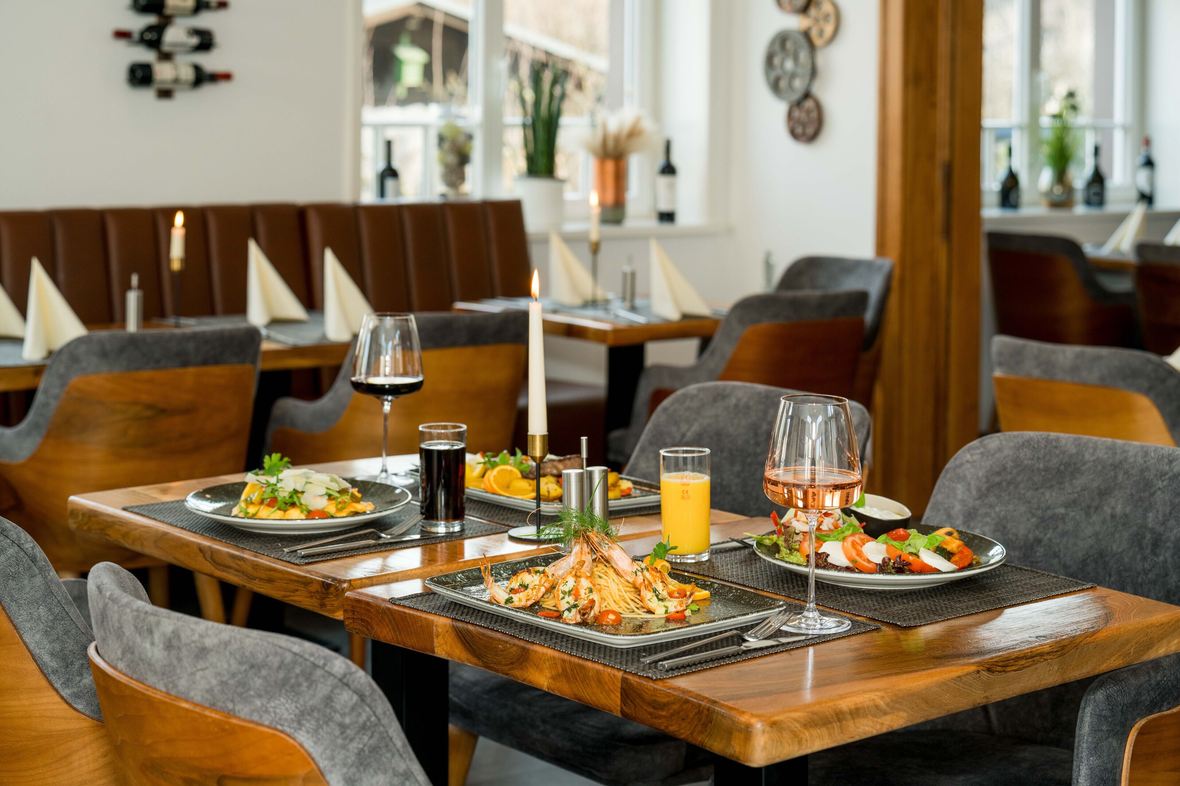 A restaurant setting with wooden tables, grey upholstered chairs, and a variety of dishes including seafood and salads.