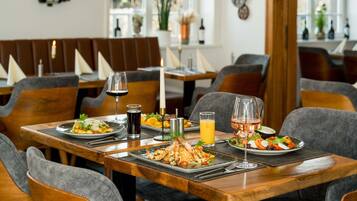 A restaurant setting with wooden tables, grey upholstered chairs, and a variety of dishes including seafood and salads.