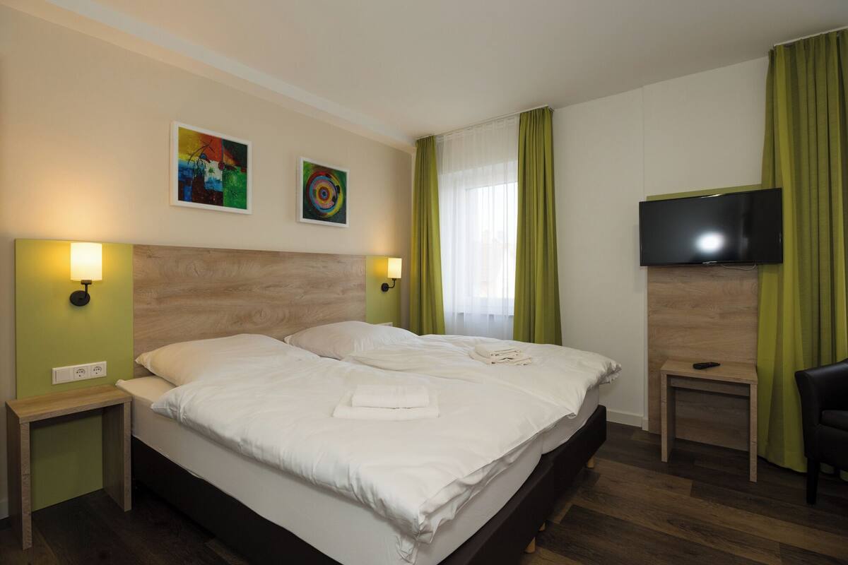 A hotel room with two beds, a flat-screen TV, and artwork on the walls.