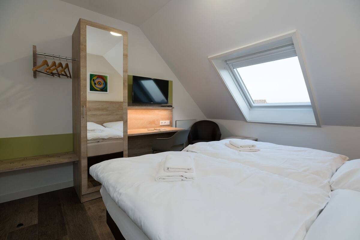 A hotel room with a bed, a desk, a chair, a TV, and a window.