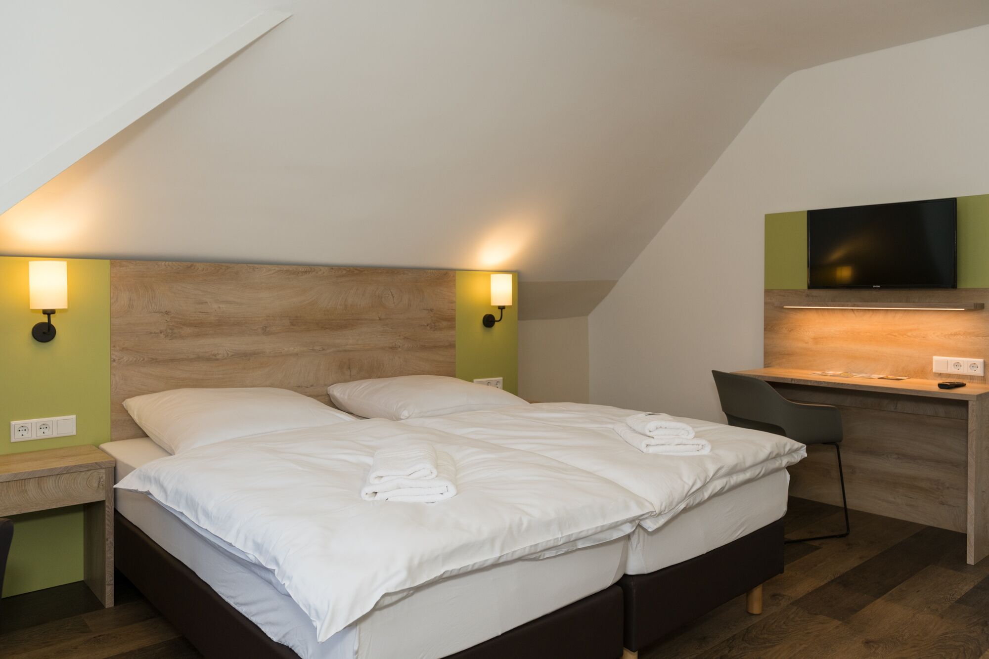 A bedroom with a bed, bedside tables, a desk, and a TV.