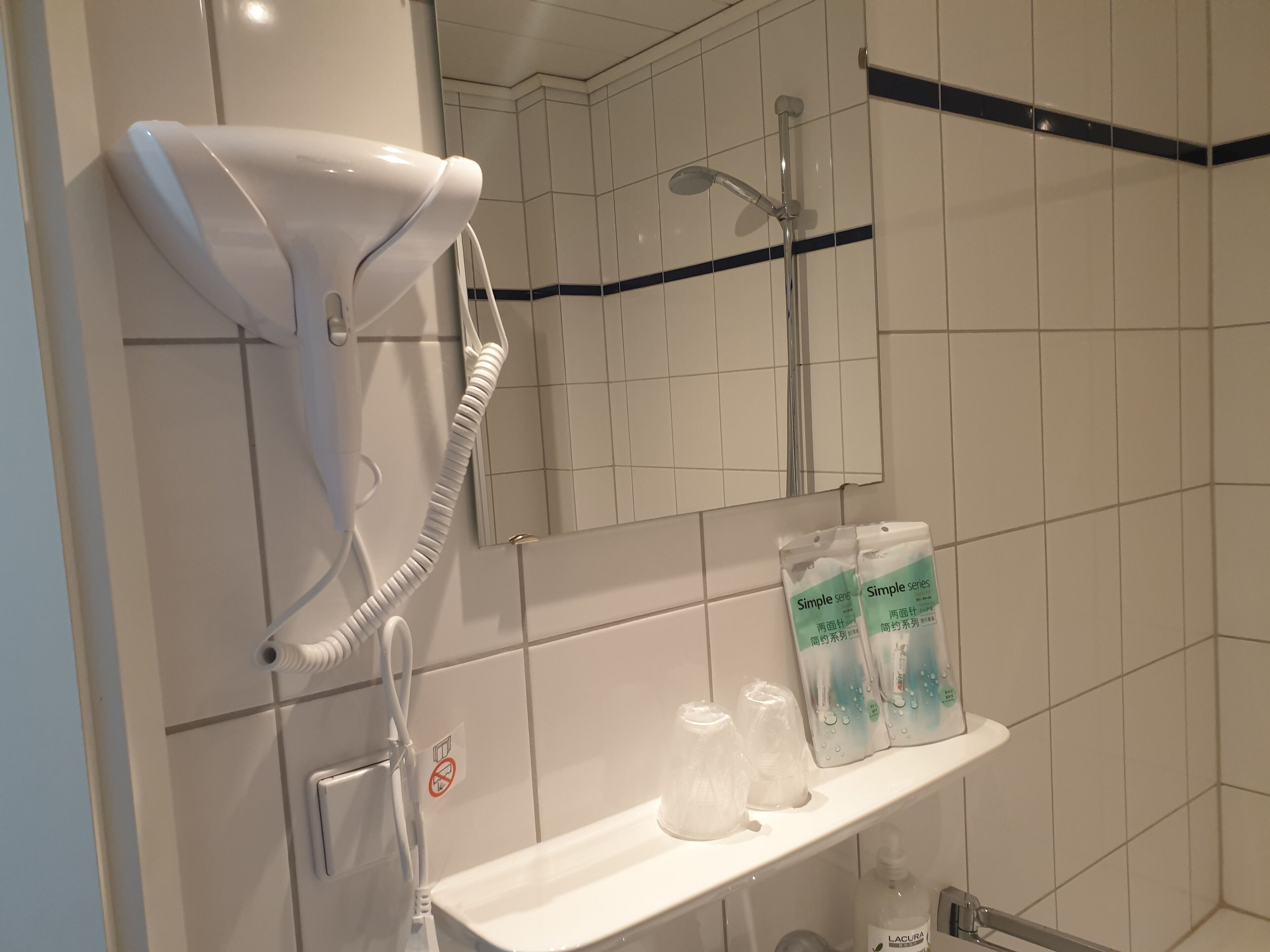 A bathroom with a hairdryer, a shower, a towel rack, and toiletries on a shelf.
