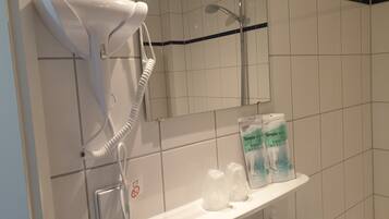 A bathroom with a hairdryer, a shower, a towel rack, and toiletries on a shelf.