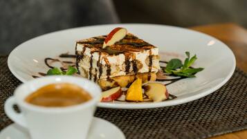A dessert plate with a slice of cake, fruit, and chocolate drizzle on a white plate, accompanied by a cup of coffee.
