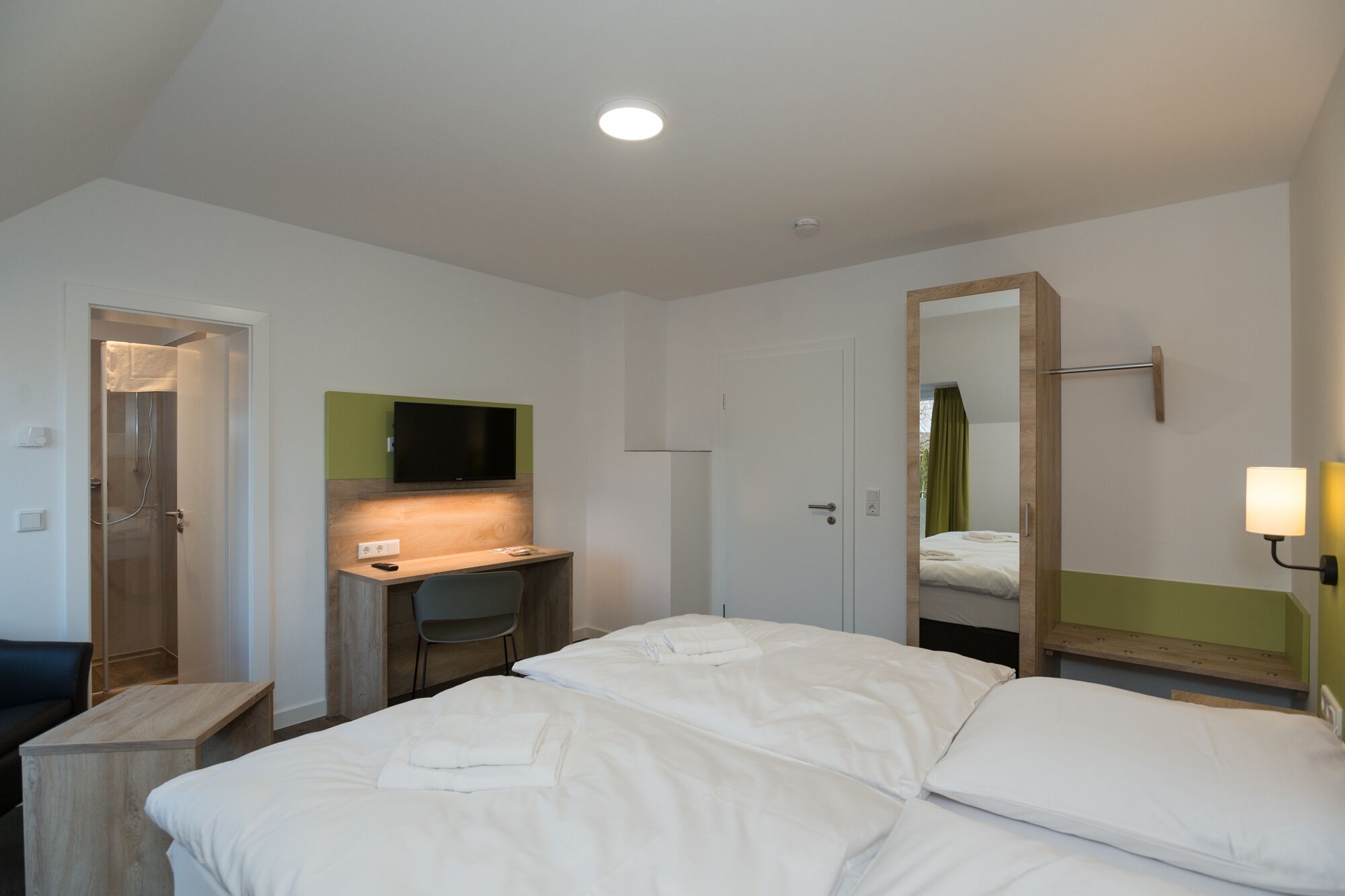 A hotel room with a bed, a desk with a chair, a television, and a mirror.