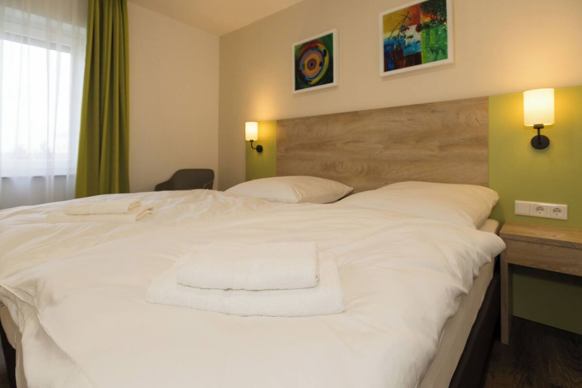 A neatly made bed with pillows and a folded towel, a chair, and two wall-mounted lamps.