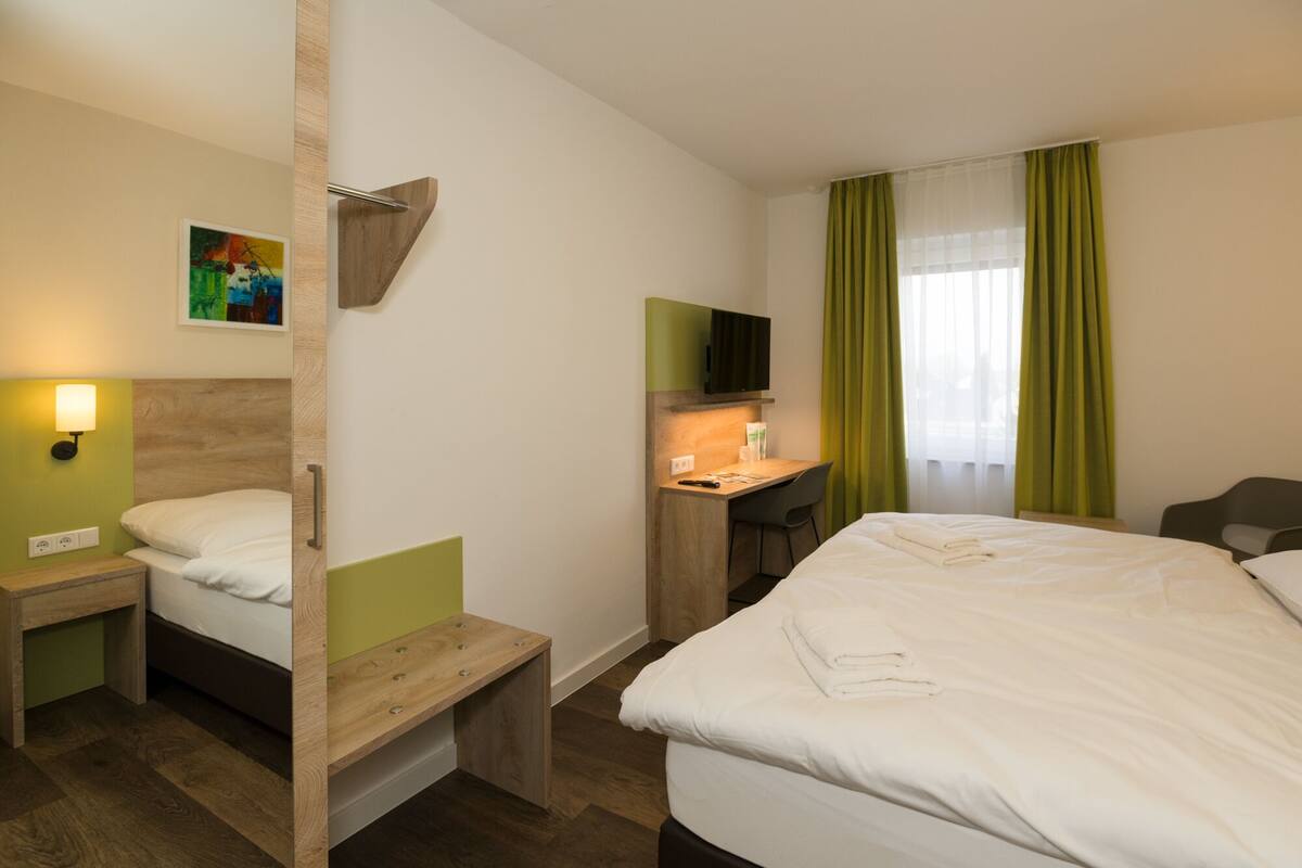 A hotel room with a bed, a desk, a chair, a TV, and a painting on the wall.