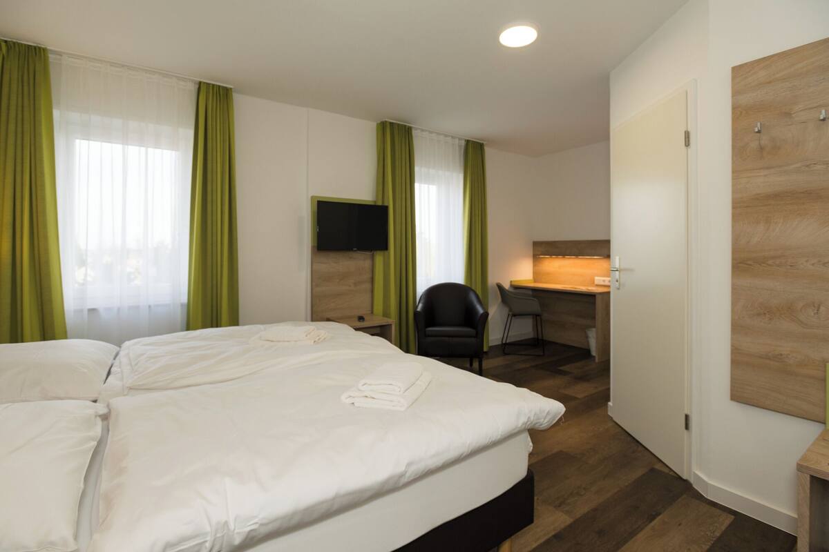 A hotel room with a bed, a desk, a chair, and a TV.