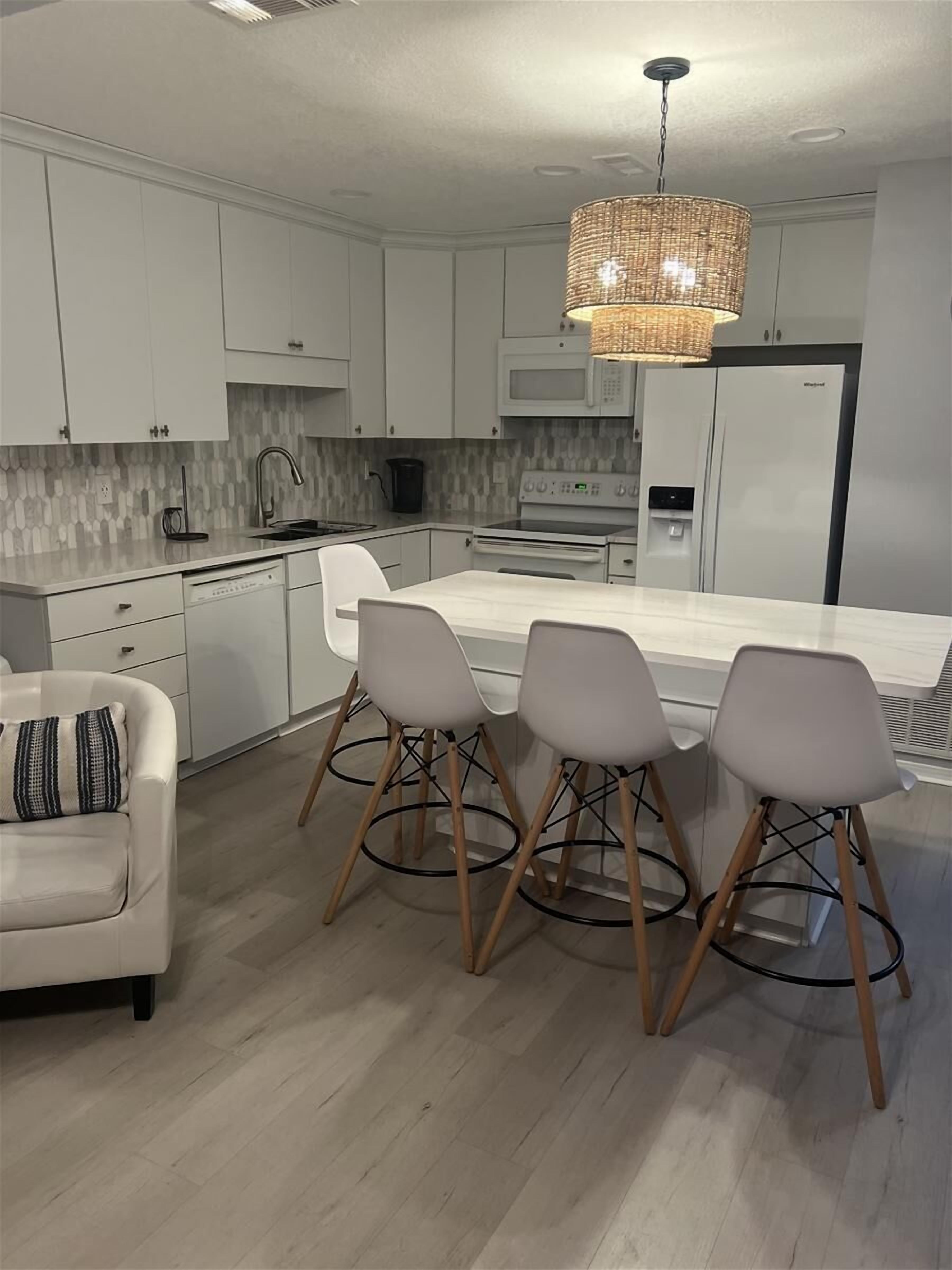 A modern kitchen with white cabinetry, a central island with bar stools, a hanging light fixture, and a built-in microwave.