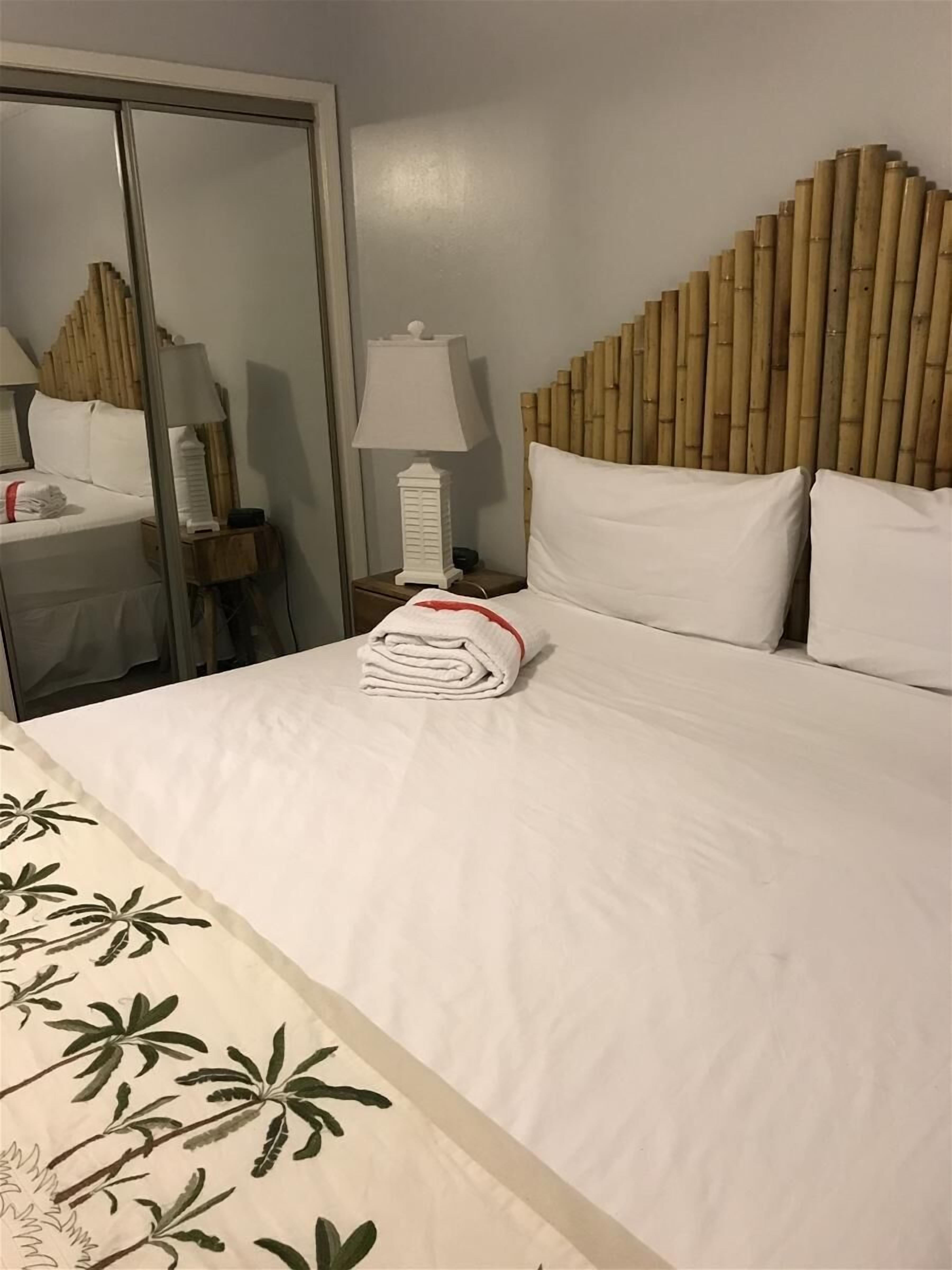 A hotel room with a bed, a nightstand with a lamp, a wooden headboard, and a mirror.