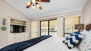 A bedroom with a bed, a TV, a ceiling fan, and a balcony with curtains. - Meet Me at The Gulf (Destin)