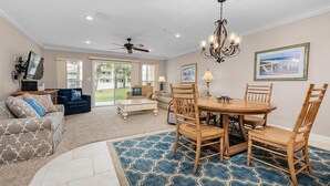 A spacious living room with a dining area, featuring a large window, ceiling fan, and a chandelier. - Meet Me at The Gulf (Destin)