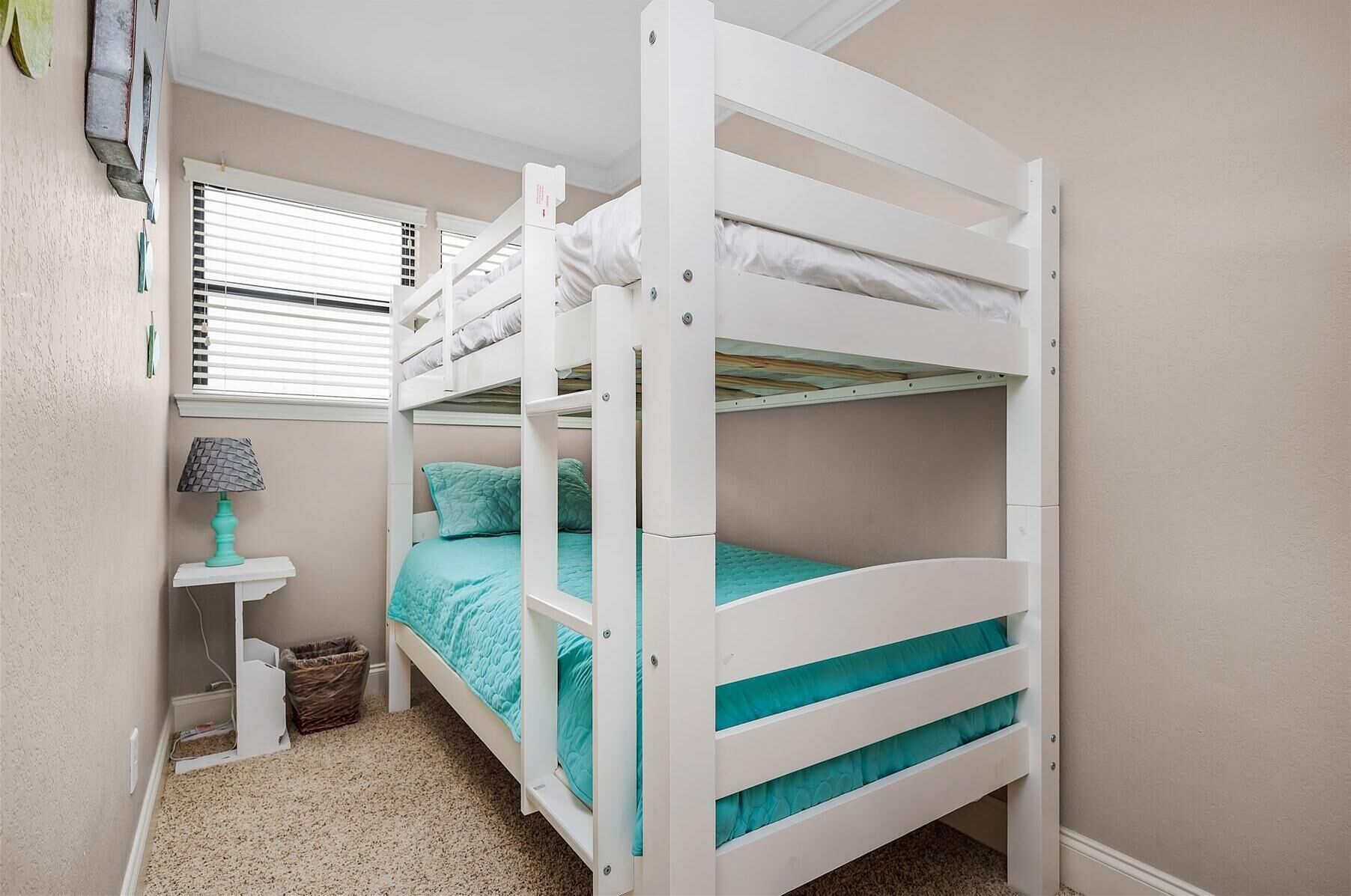 A bunk bed room with a window, a small table, and a lamp.