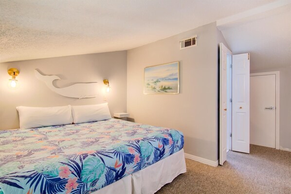 A bedroom with a large bed, a painting on the wall, and a door to another room. - 7F Nama-stay (Miramar Beach)