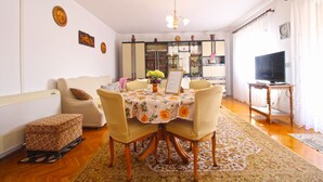Un coin repas avec une table dressée pour quatre personnes, entourée de chaises, d’un canapé et d’un téléviseur posé sur un meuble.