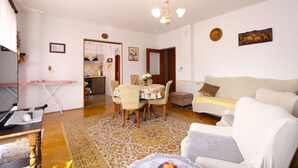 Un salon confortable avec un canapé, une table à manger et des chaises, un coin cuisine et un lustre.